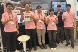 台灣創新展，六名參展團隊成員於豬隻瘦肉量檢測系統展位前合影，其中一人手持技術介紹資料。